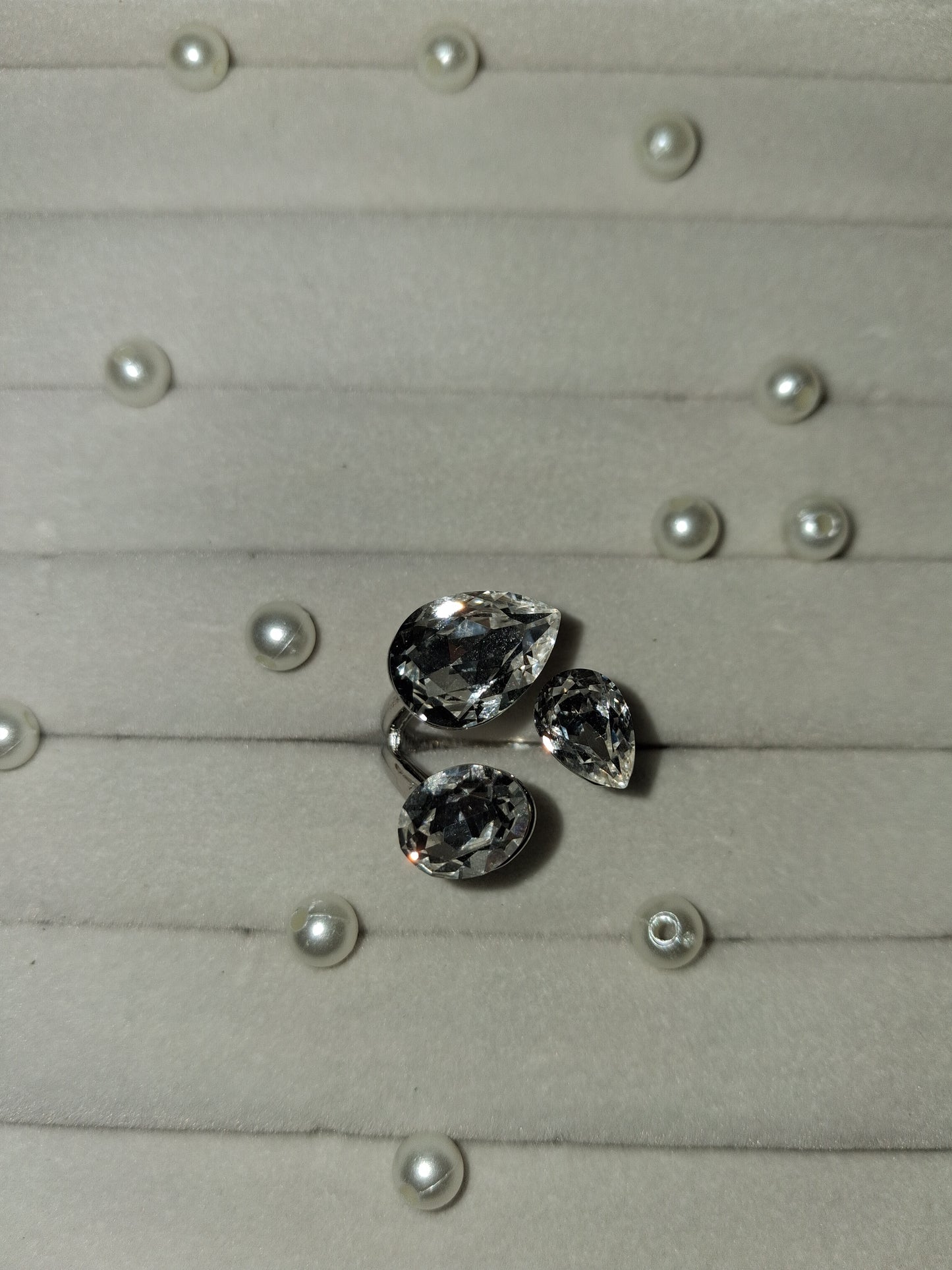 Three loose teardrop-shaped clear gemstones arranged on a light gray display surface with small pearl-like studs.