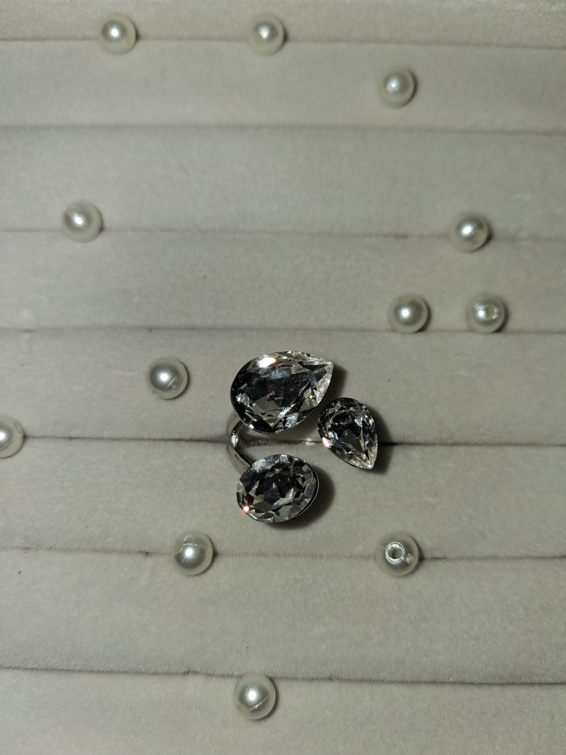 Three loose teardrop-shaped clear gemstones arranged on a light gray display surface with small pearl-like studs.