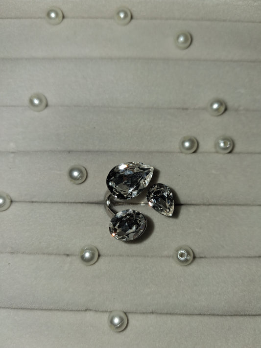 Three loose teardrop-shaped clear gemstones arranged on a light gray display surface with small pearl-like studs.